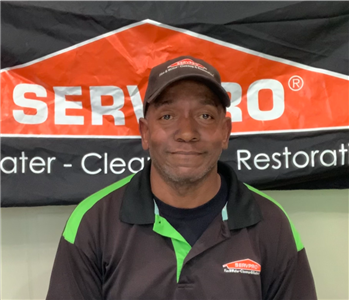 male employee with black hat smiling in in front of SERVPRO sign